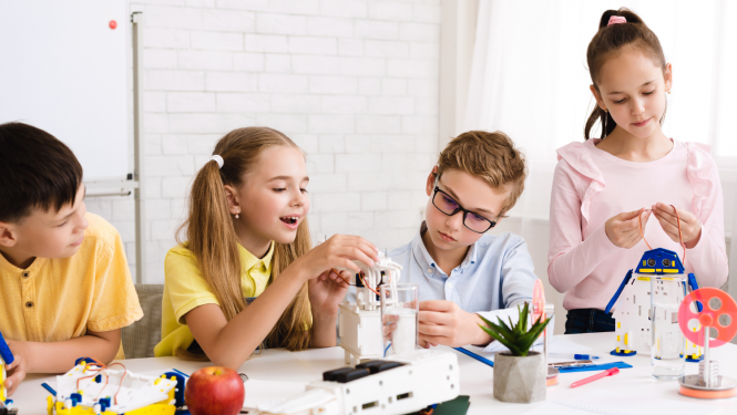 4 bērni pie galda būvē no plastmasas elektroniski darbināmu ierīci