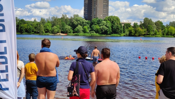 Cilvēki stāv pie Daugavas, viens cilvēks ir glābšanas vestē ūdenī