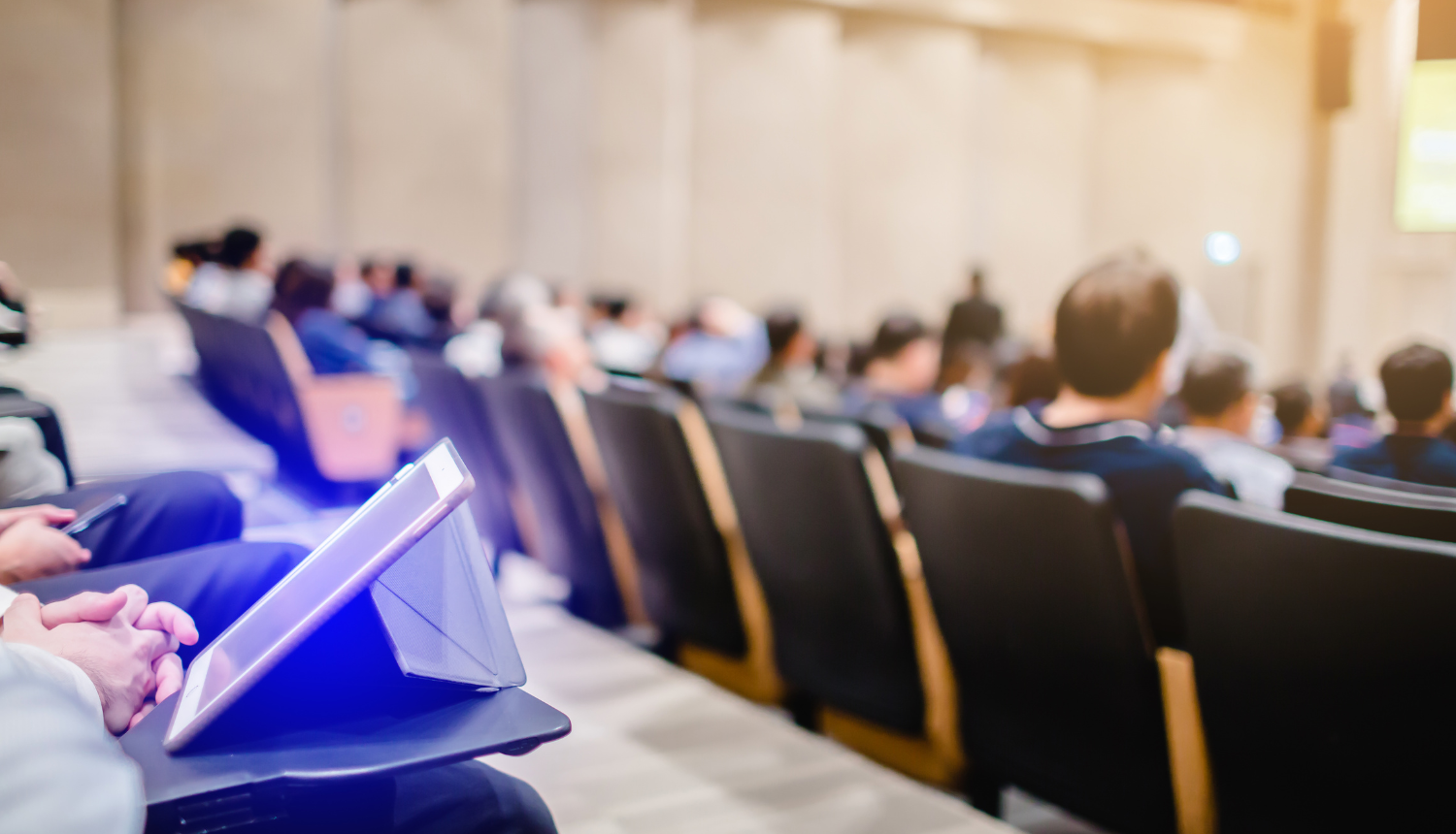 Auditorija ar studentiem, uz galda stāv planšetdators.