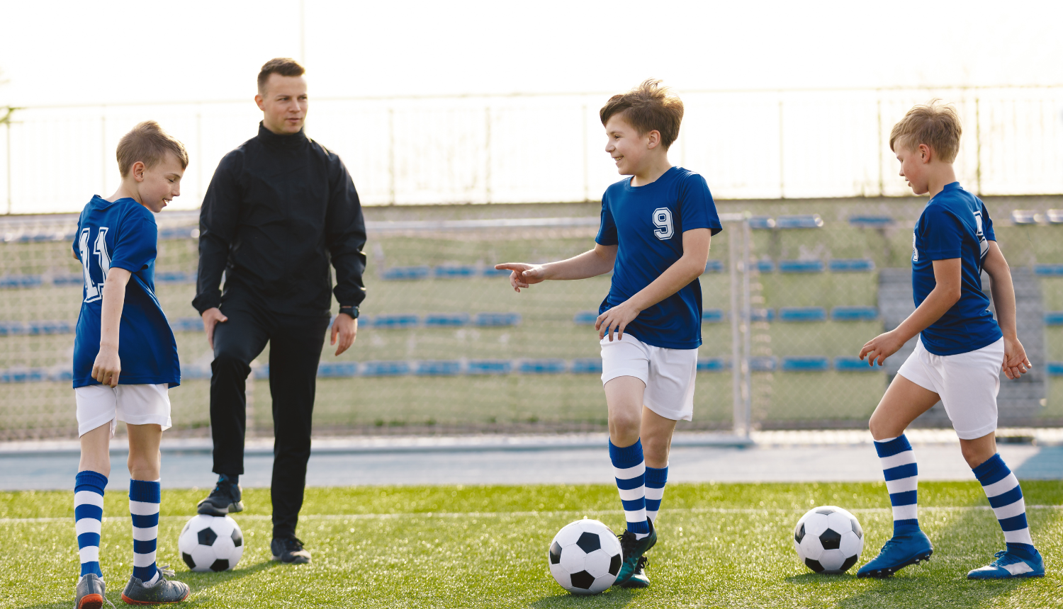 Treneris futbola laukumā kopā ar 2 zēniem un futbola bumbām