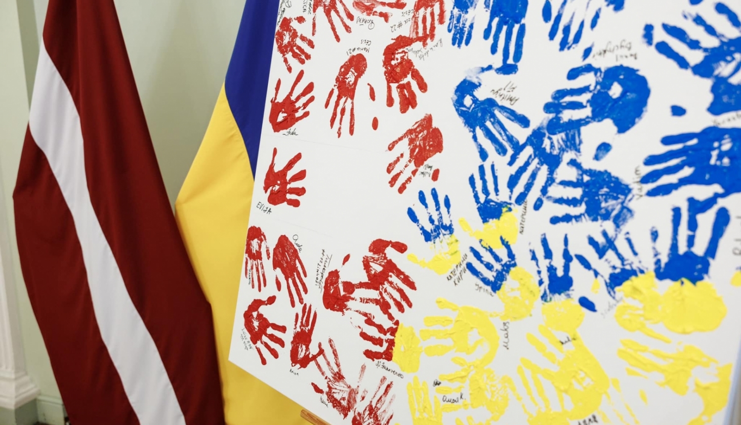 Latvijas un Ukrainas karogi, priekšplānās balts audekls ar krāsā iemērktiem rokas nospiedumiem sarkanā, zilā un dzeltenā krāsā